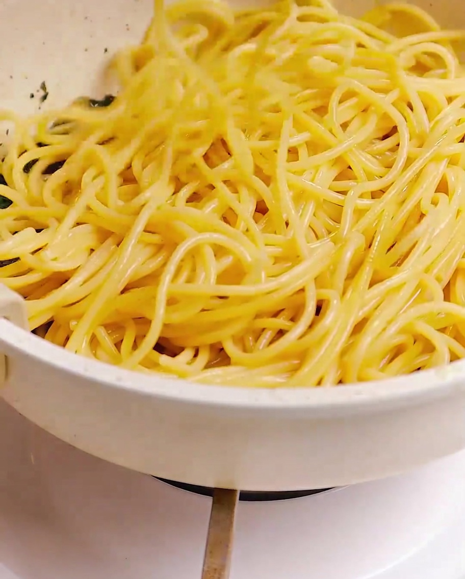 Spaghetti cuits mélangés dans une poêle avec un mélange de bacon, dail et dherbes à laide de baguettes.