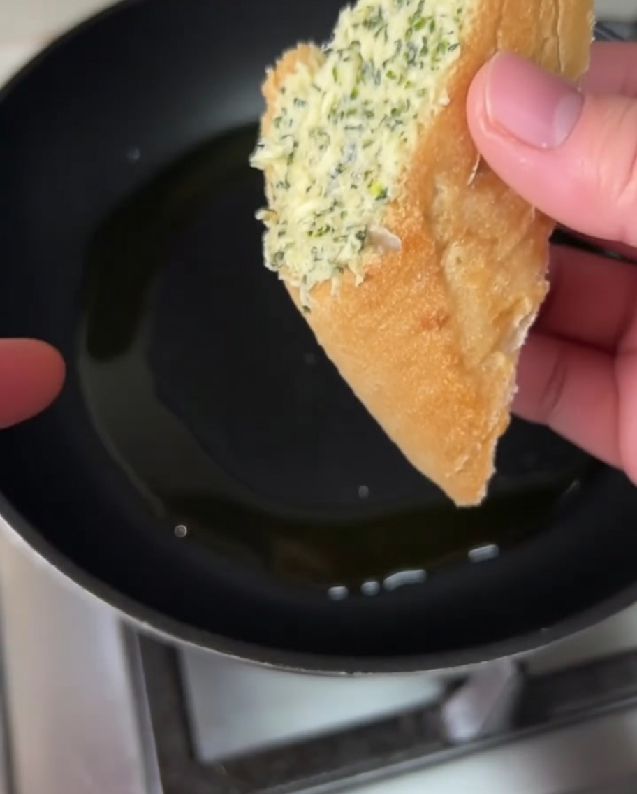 Tranches de pain tartinées de beurre à lail en train de dorer dans une poêle avec de lhuile dolive.