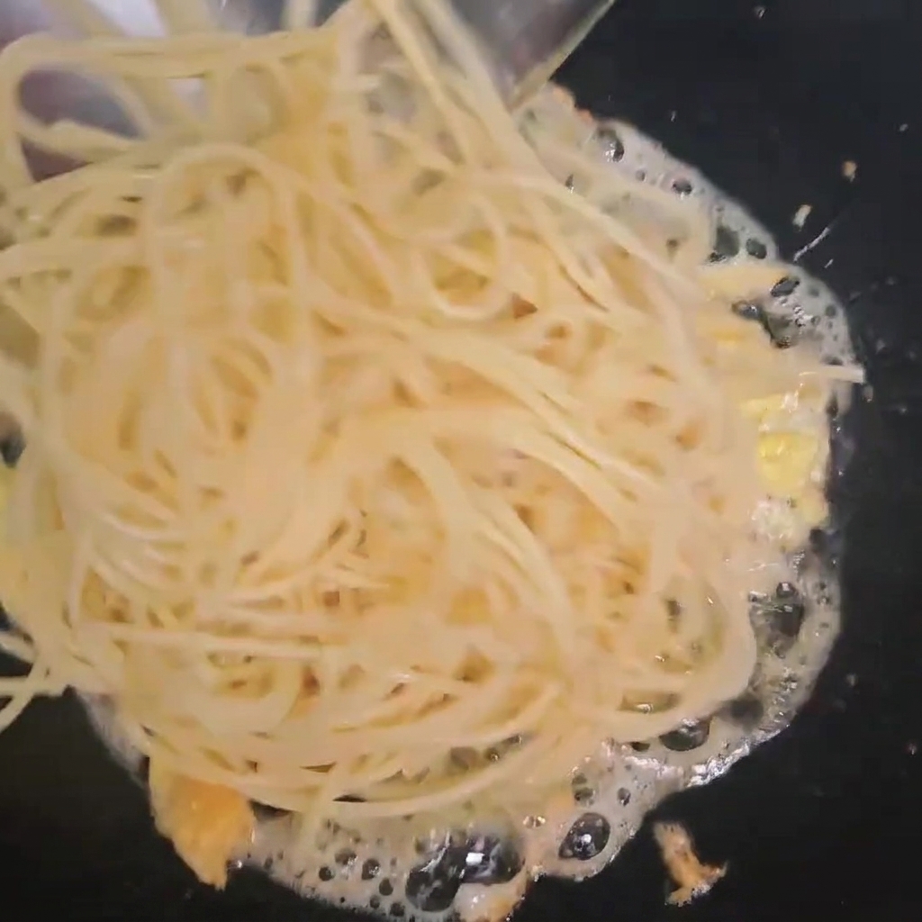 Spaghettis cuits ajoutés dans un wok contenant les œufs brouillés.