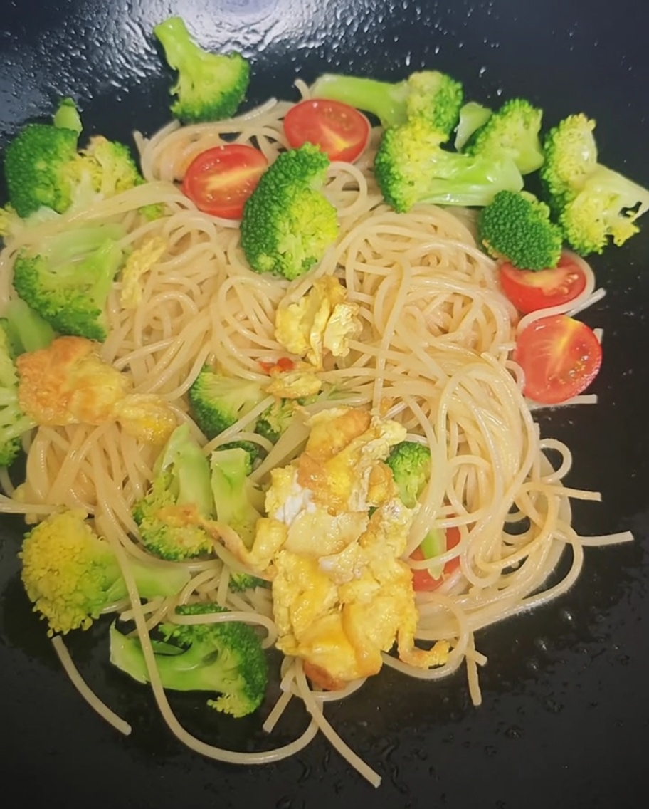 Assaisonnement saupoudré depuis un sachet sur les spaghettis, le brocoli et les tomates cerises dans un wok.