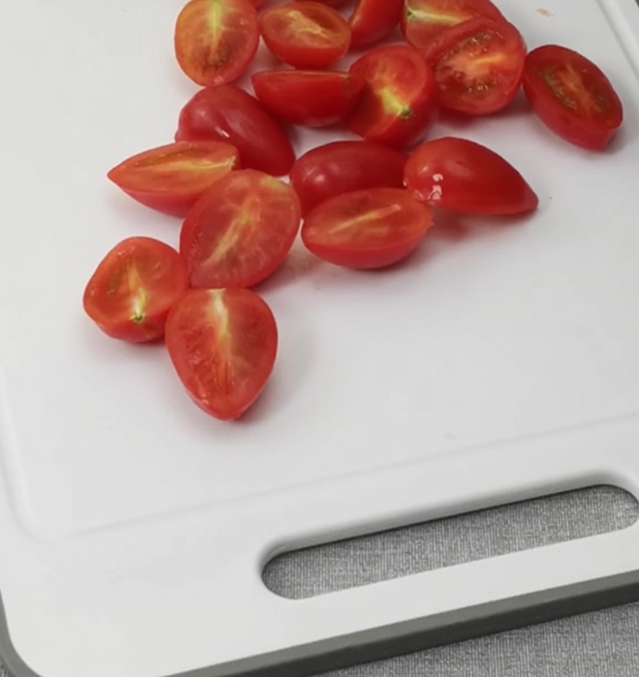Tomates cerises coupées en deux sur une planche à découper blanche.
