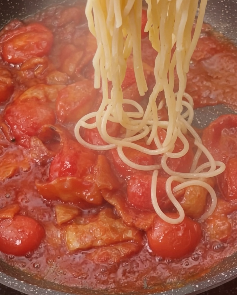 Pâtes cuites ajoutées dans la poêle contenant la sauce au bacon et tomate.