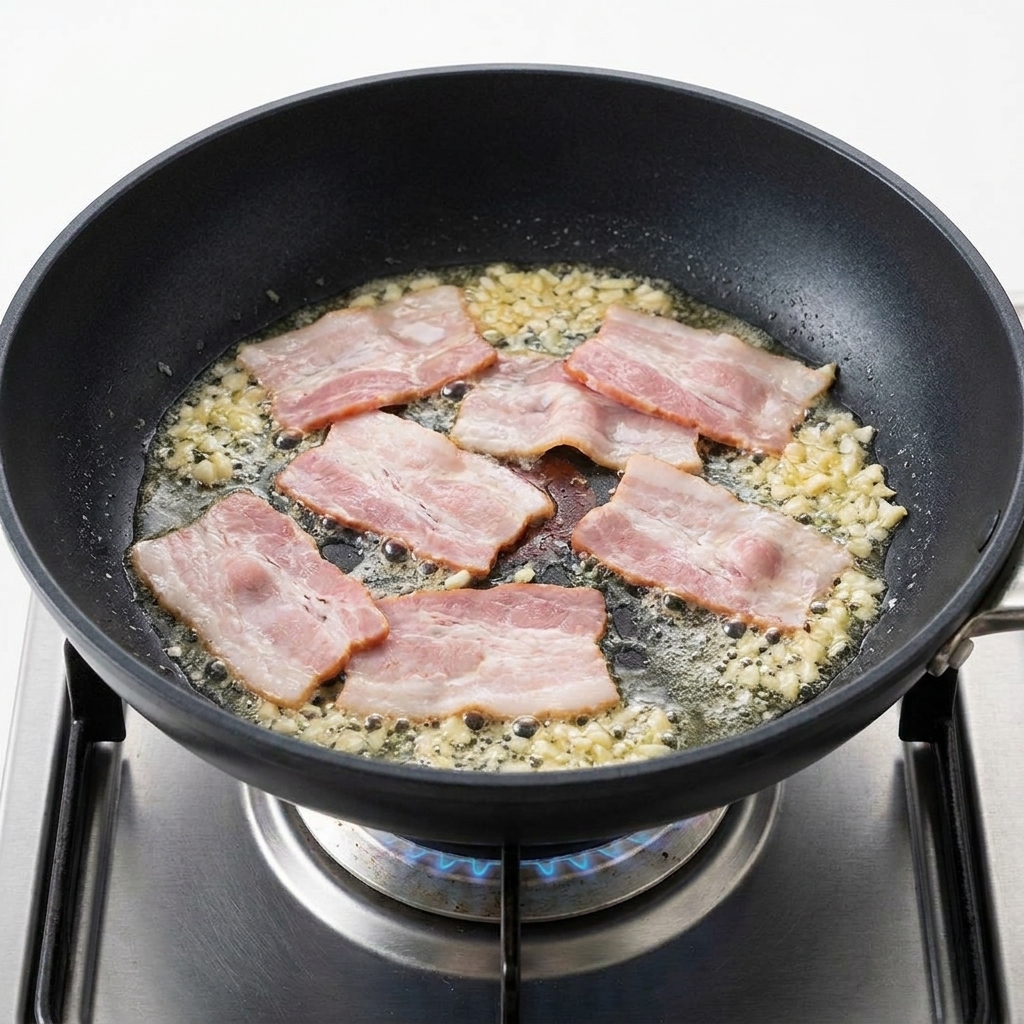 Morceaux de bacon grésillant dans une poêle avec de lail doré parfumé.