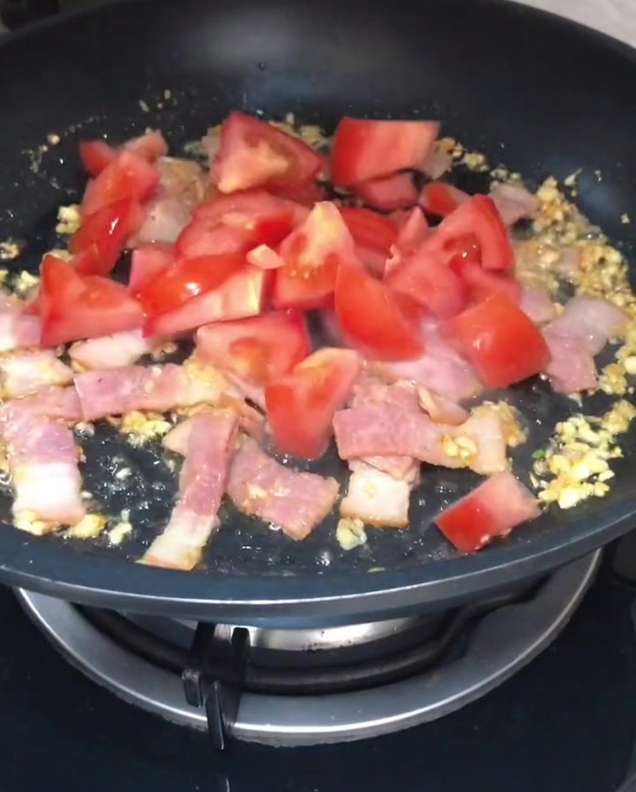 Morceaux de tomate rouge fraîche ajoutés au bacon et à lail dans la poêle.