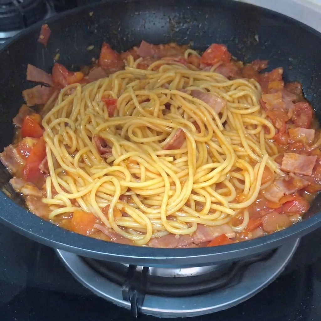 Gros plan sur les pâtes mélangées dans une poêle avec la sauce, du poivre noir étant saupoudré par-dessus.