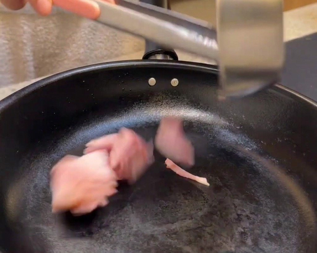 Ajout des morceaux de bacon dans une poêle noire pour les faire dorer.