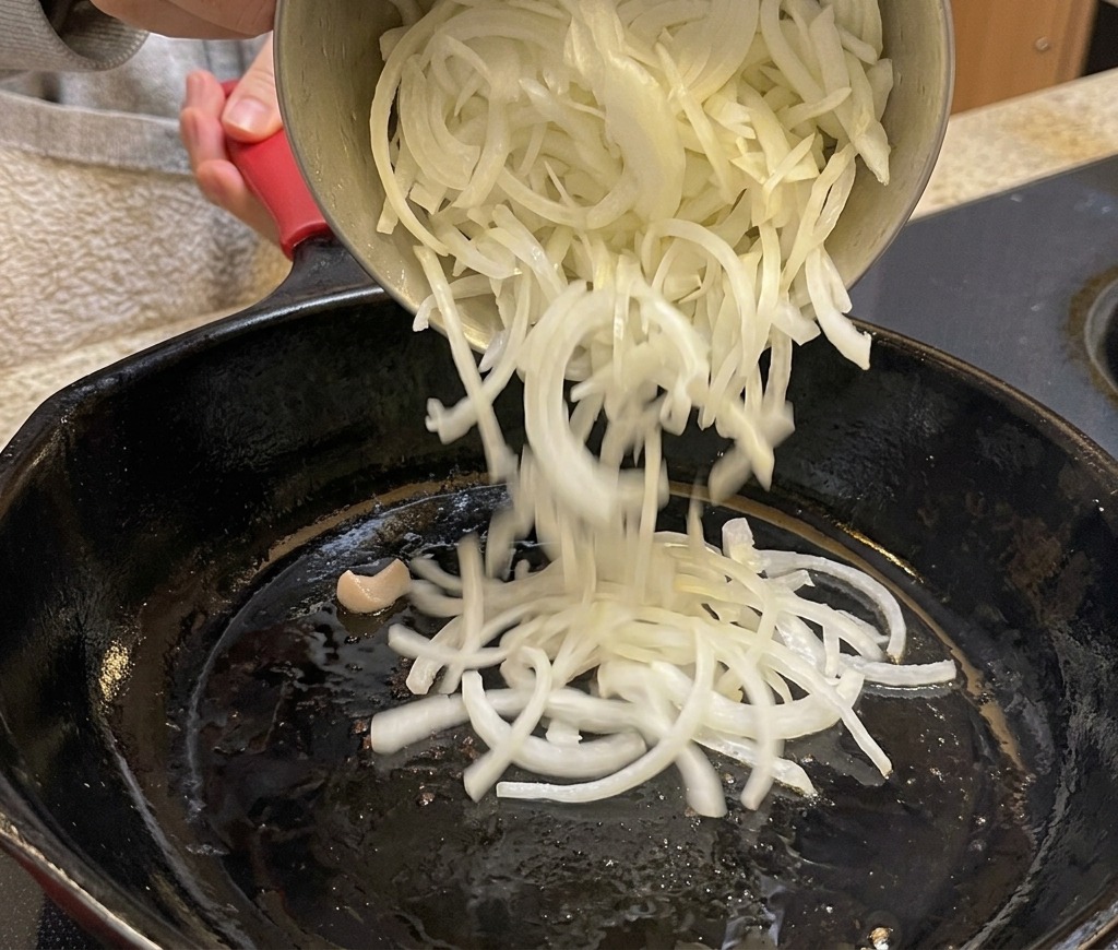Ajout des oignons émincés dans une poêle noire avec le bacon.