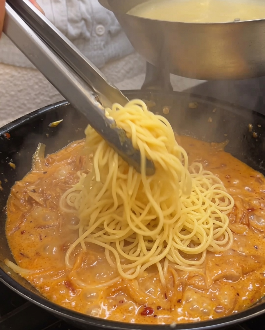 Mélange des spaghettis dans la sauce crémeuse à laide dune pince.