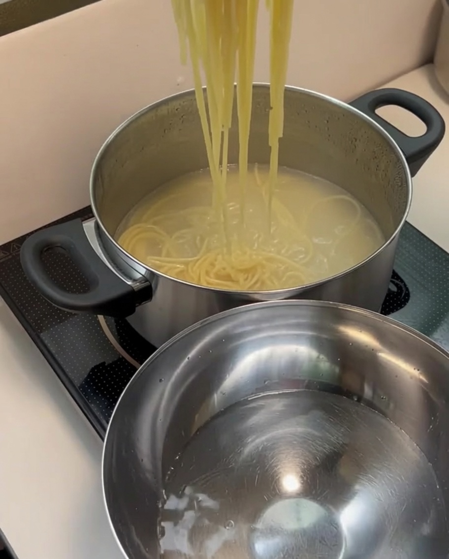 Des spaghettis cuits égouttés transférés dans un bol en inox contenant de leau froide claire.