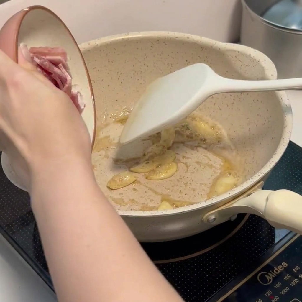 De petits morceaux de bacon haché frits dans une poêle avec des lamelles dail parfumées.