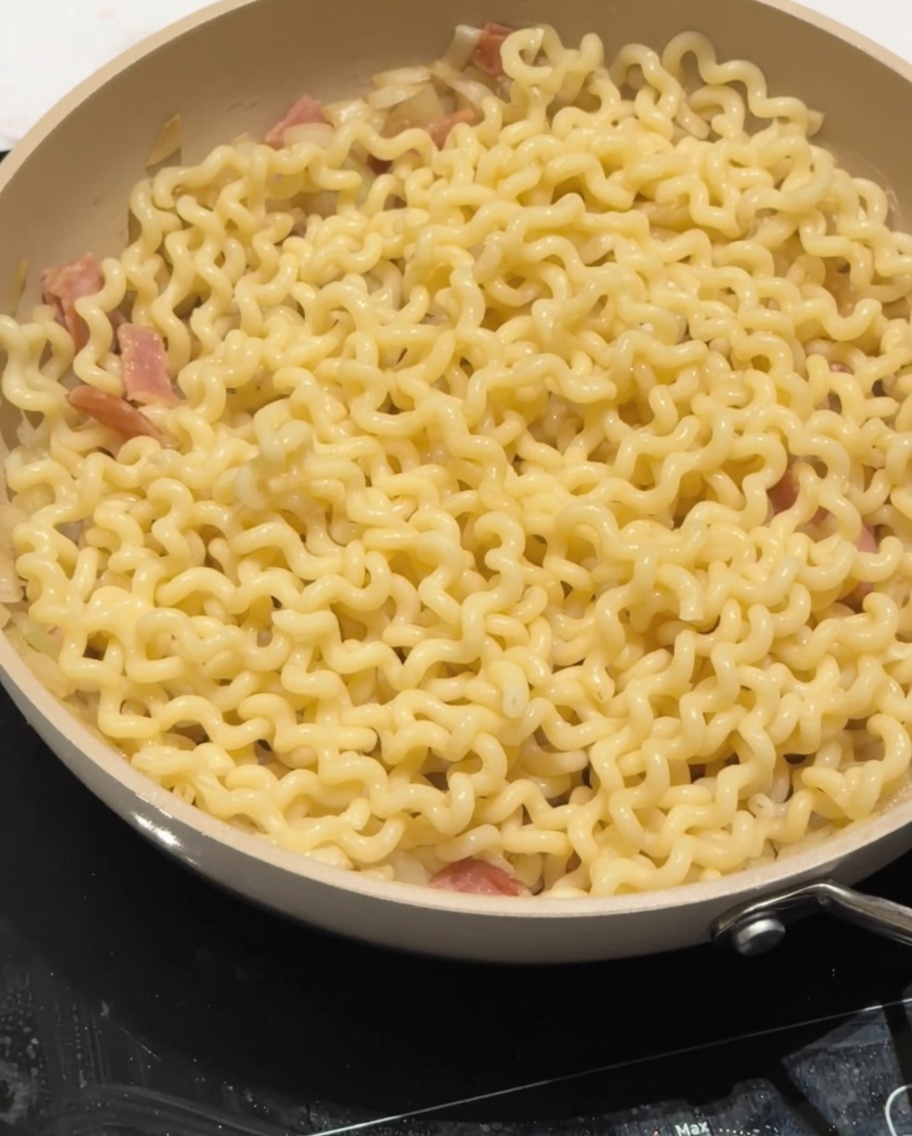 Du lait demi-écrémé versé sur les nouilles dans la poêle.