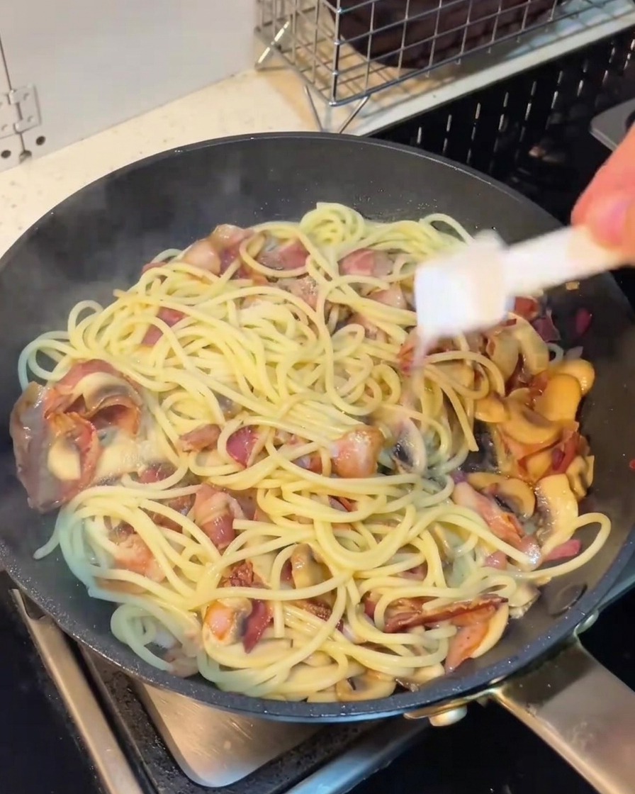 Main saupoudrant du poivre sur les spaghettis dans la poêle.
