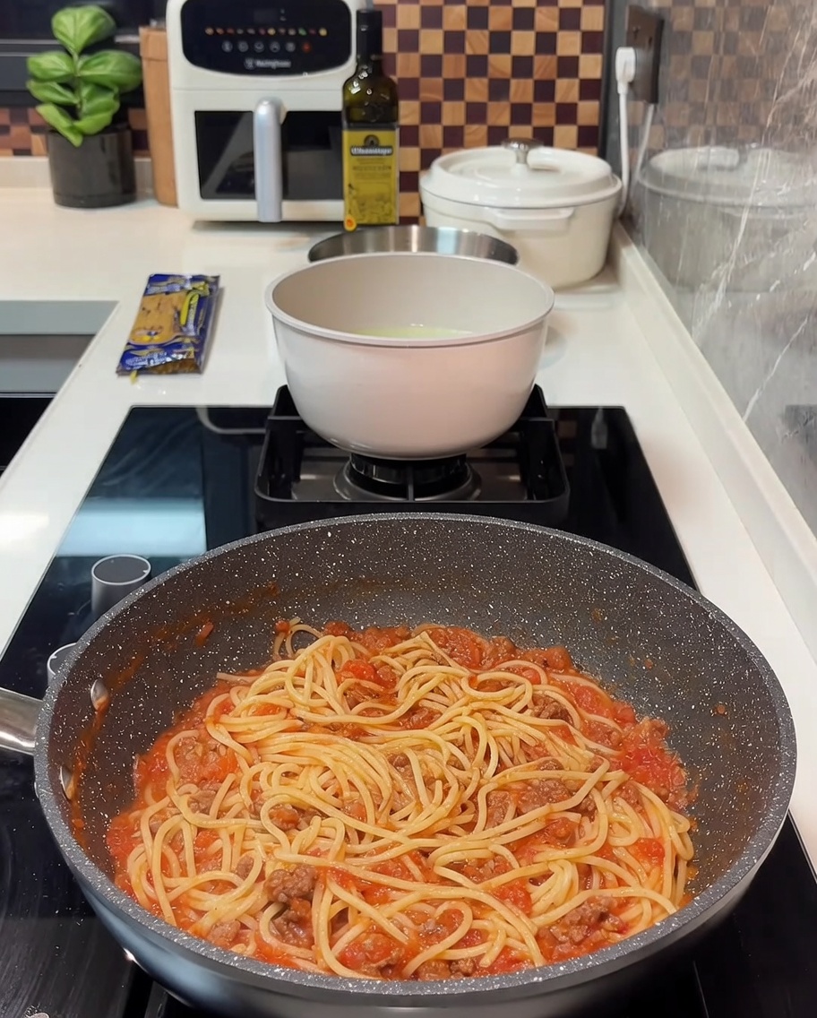Une poêle remplie de spaghettis à la sauce à la viande, recouverte de quelques tranches de fromage jaune.