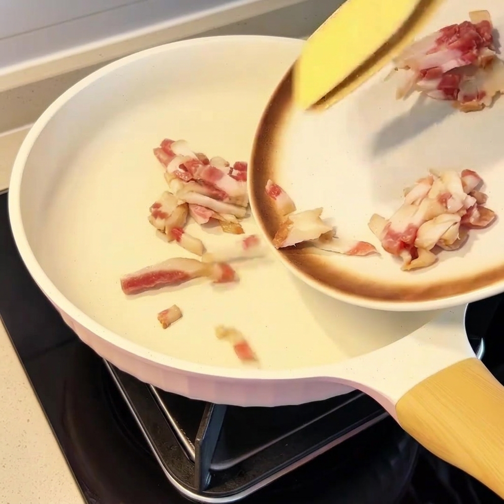 Morceaux de guanciale répartis uniformément dans une poêle froide.