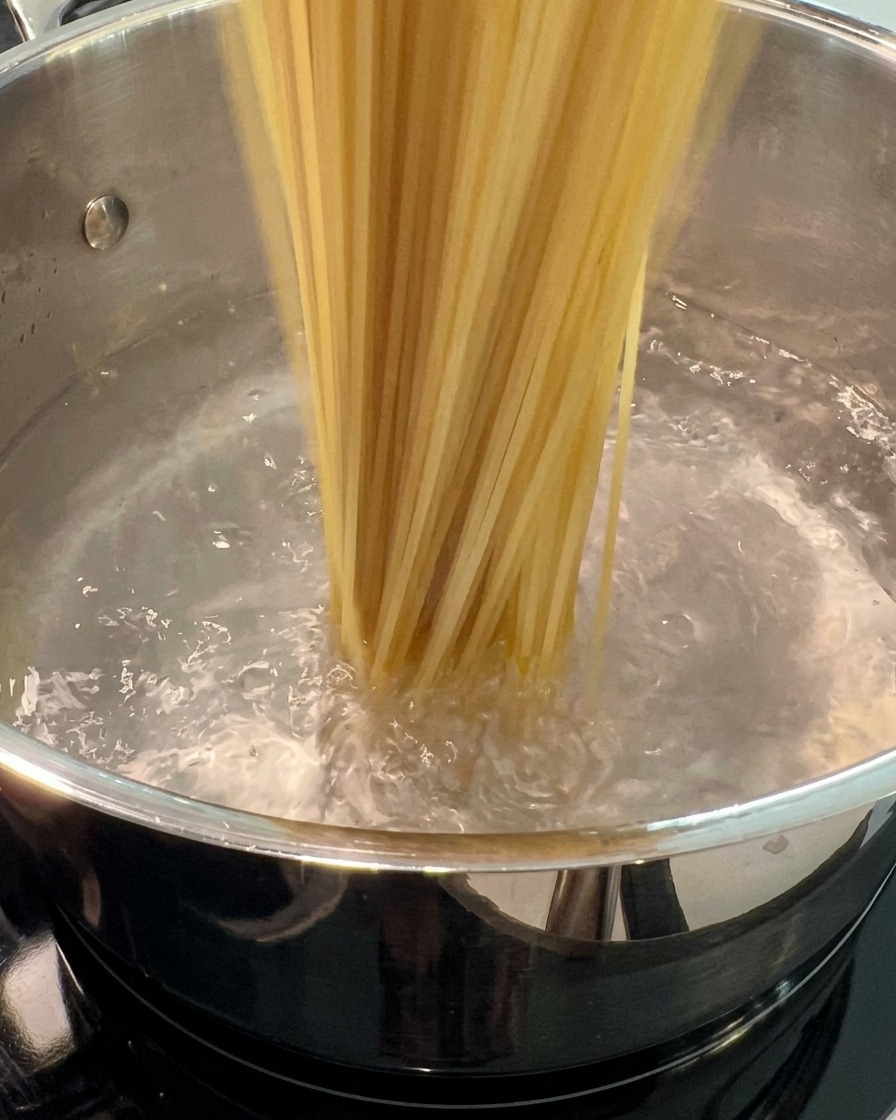 Des spaghettis secs plongés dans une grande marmite deau bouillante.