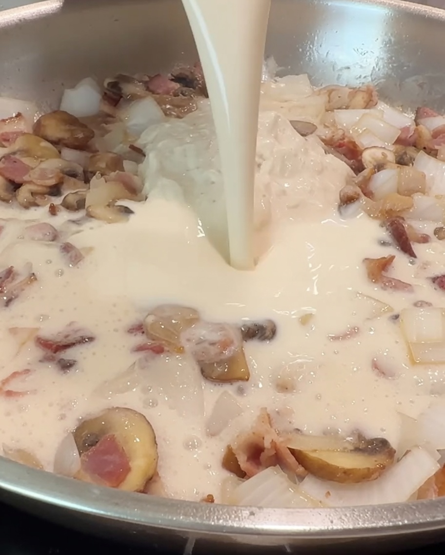 Une tasse de lait versée dans la poêle pour se mélanger à la sauce Alfredo et à la garniture.