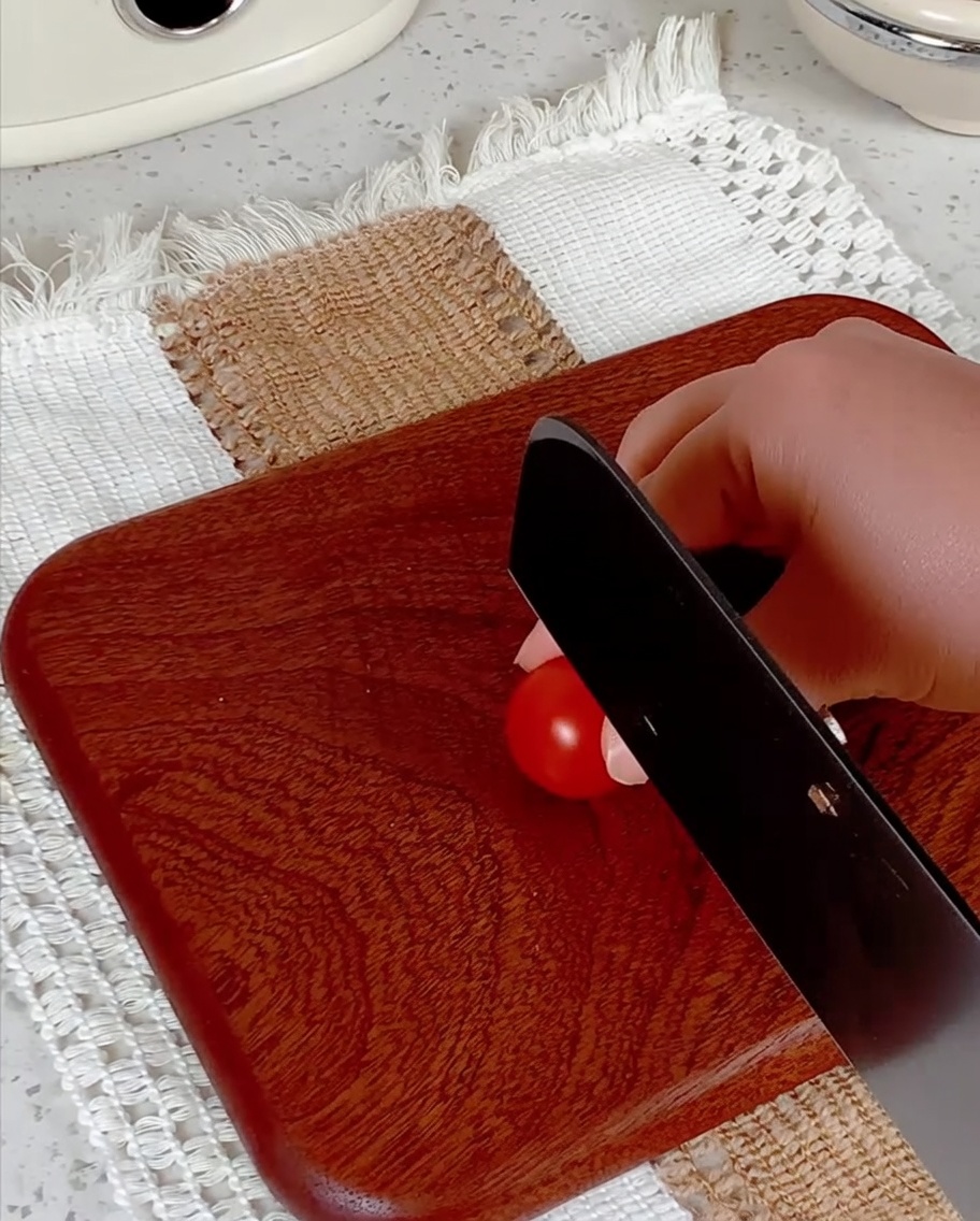 Des tomates cerises coupées en deux sur une planche à découper avec un couteau.