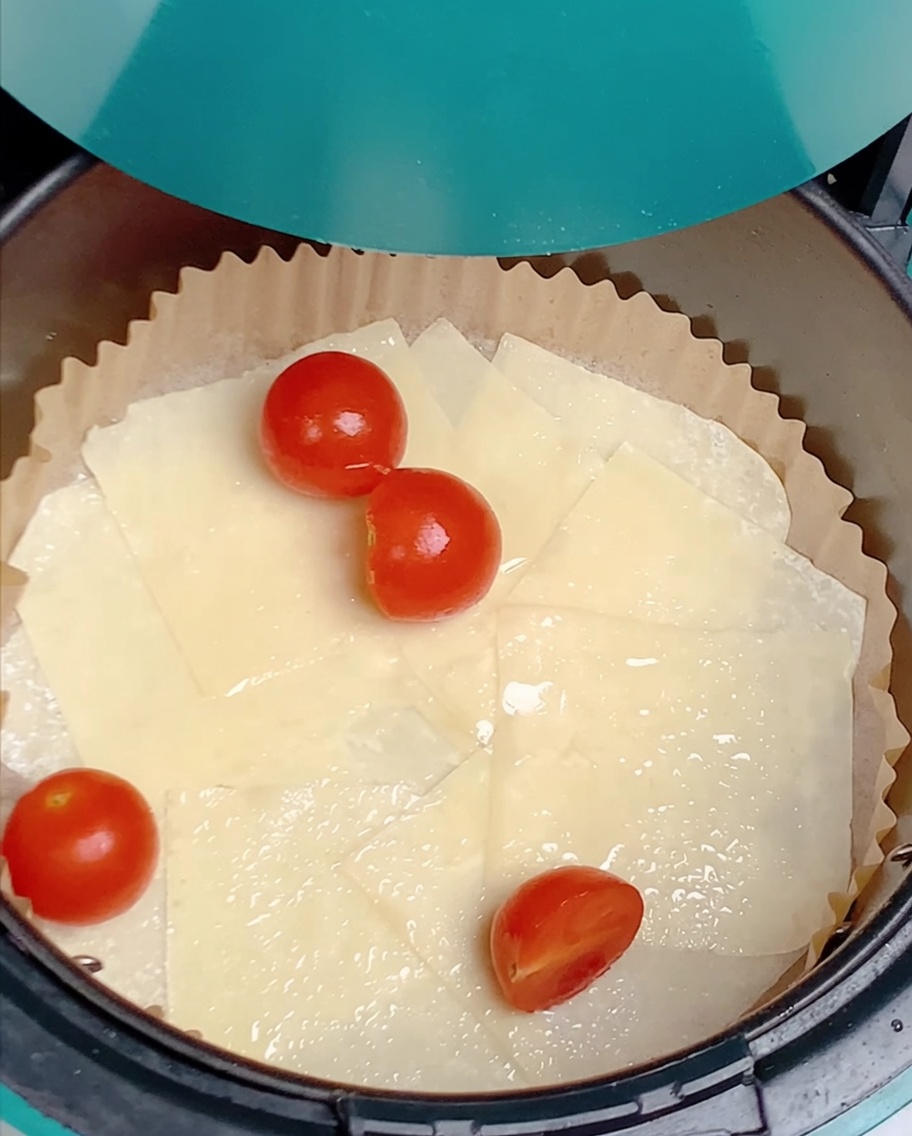 Des moitiés de tomates cerises éparpillées sur des feuilles de wonton huilées dans un panier de friteuse.