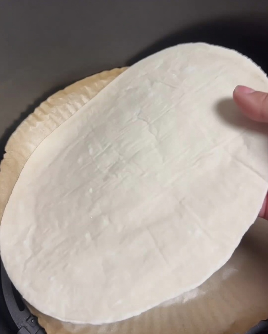 Une crêpe à la ciboule crue posée à plat dans le panier dune friteuse à air tapissé de papier sulfurisé.