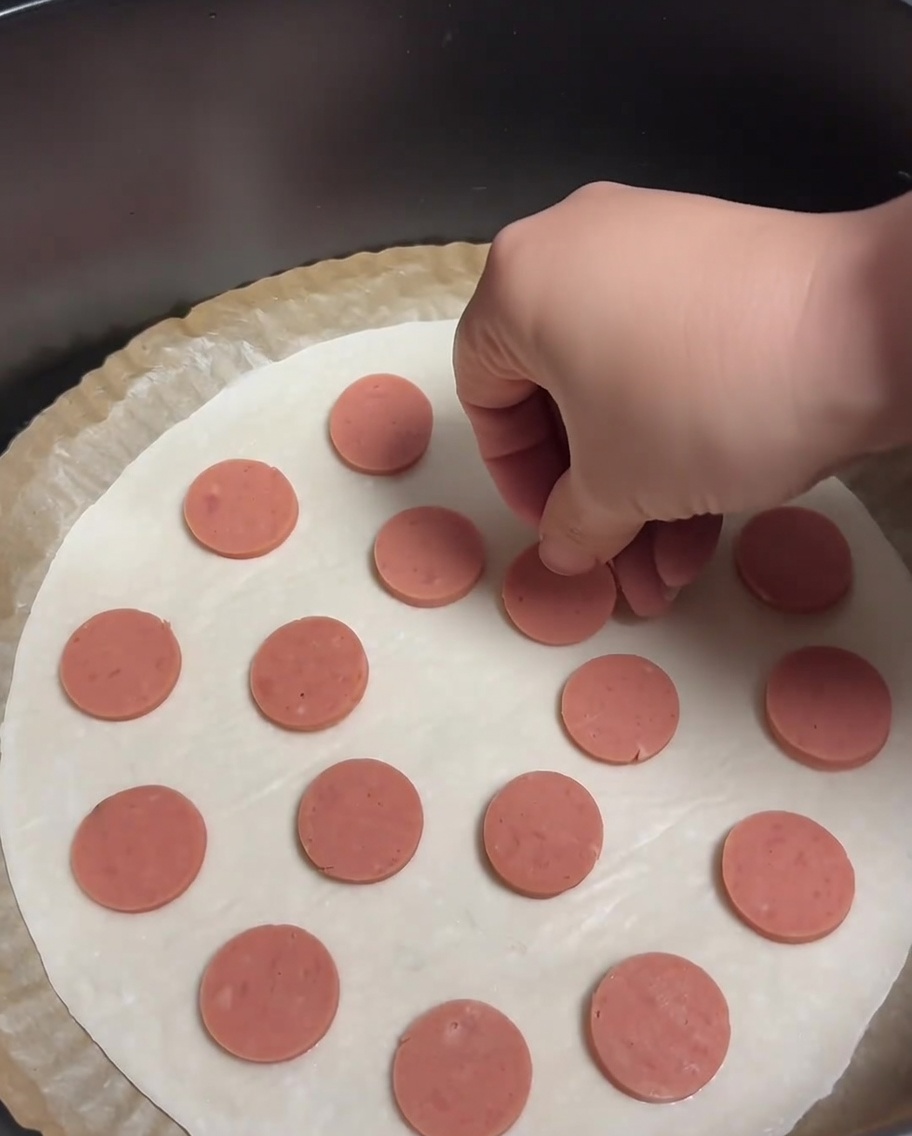 Une crêpe à la ciboule garnie de rondelles de saucisse réparties uniformément.