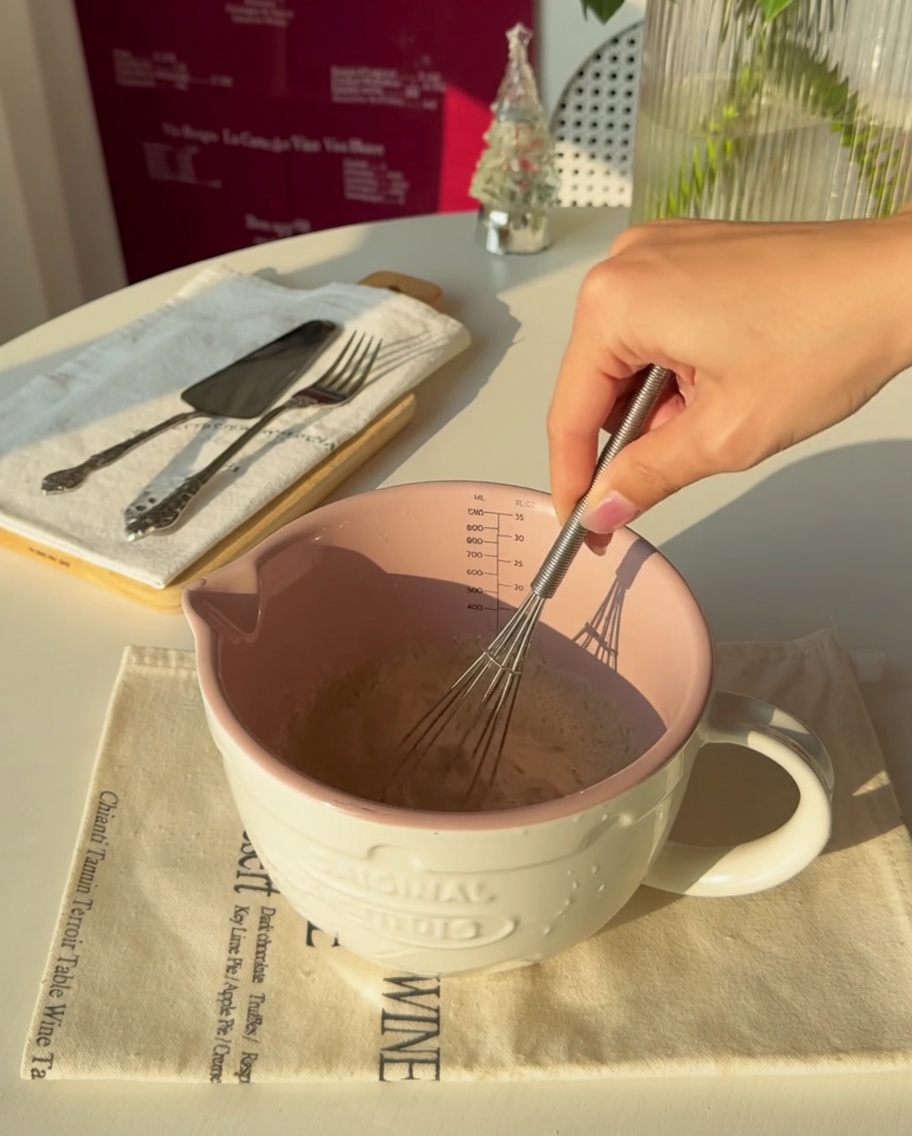 Gros plan sur une main fouettant la levure dans de leau tiède à lintérieur dune tasse à mesurer rose.