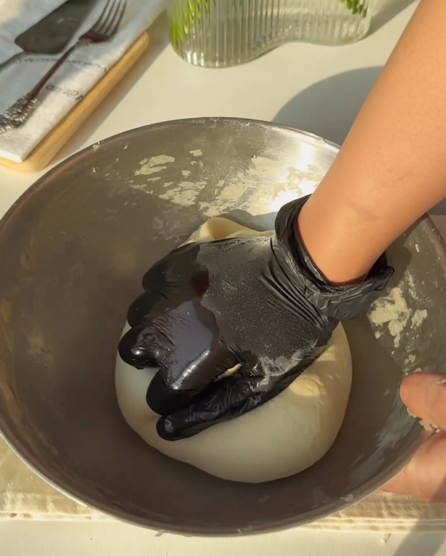 Une main gantée pétrissant fermement la pâte jusquà ce quelle soit lisse.