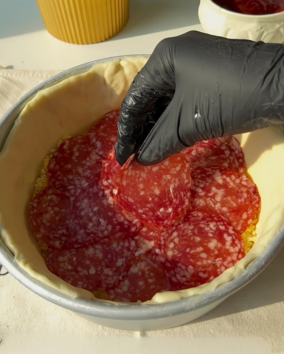 Bandes de bacon placées sur la couche de salami.