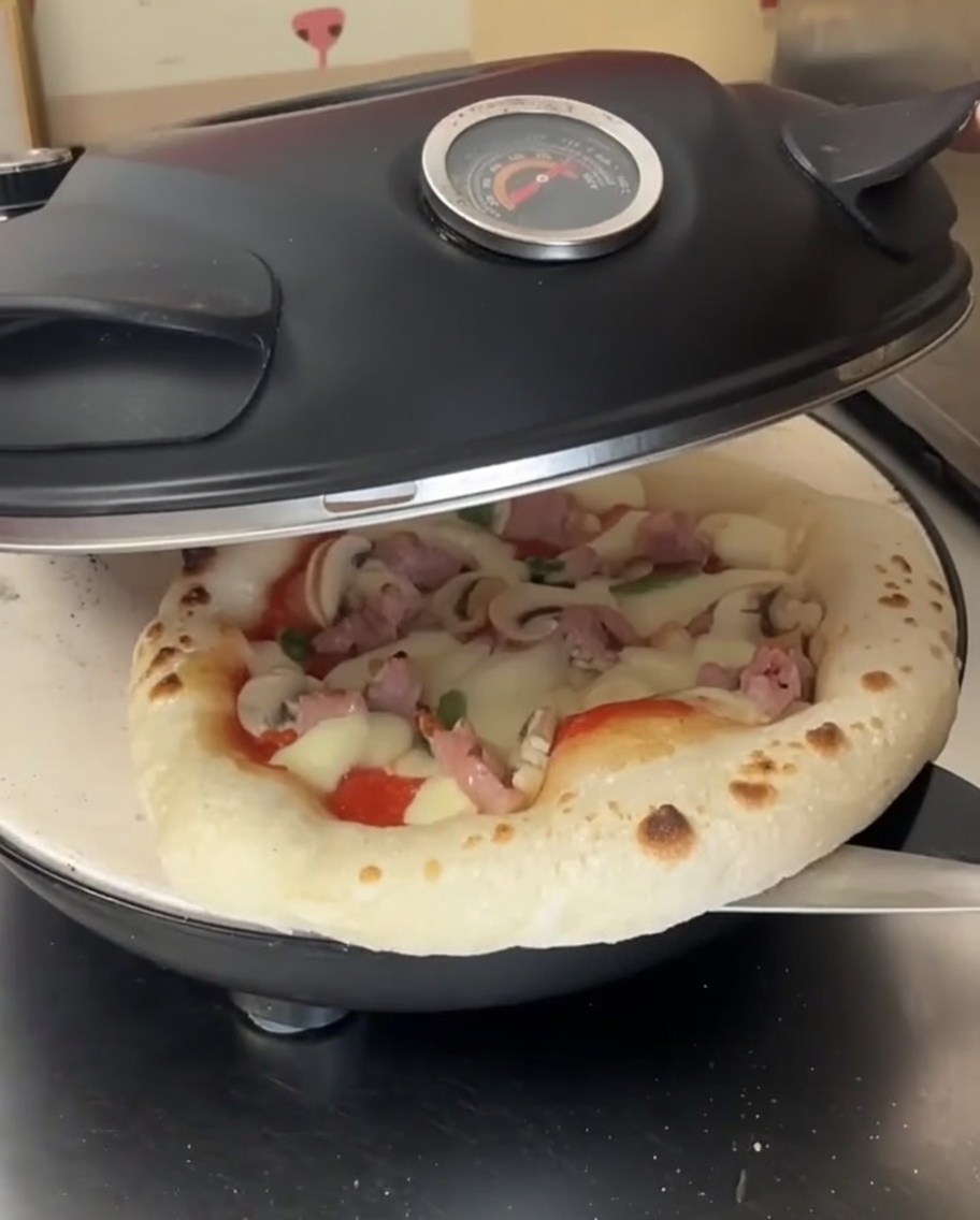 Une pizza à mi-cuisson avec du fromage fondu à lintérieur dun four ouvert, en train dêtre tournée avec une pelle à pizza en métal.