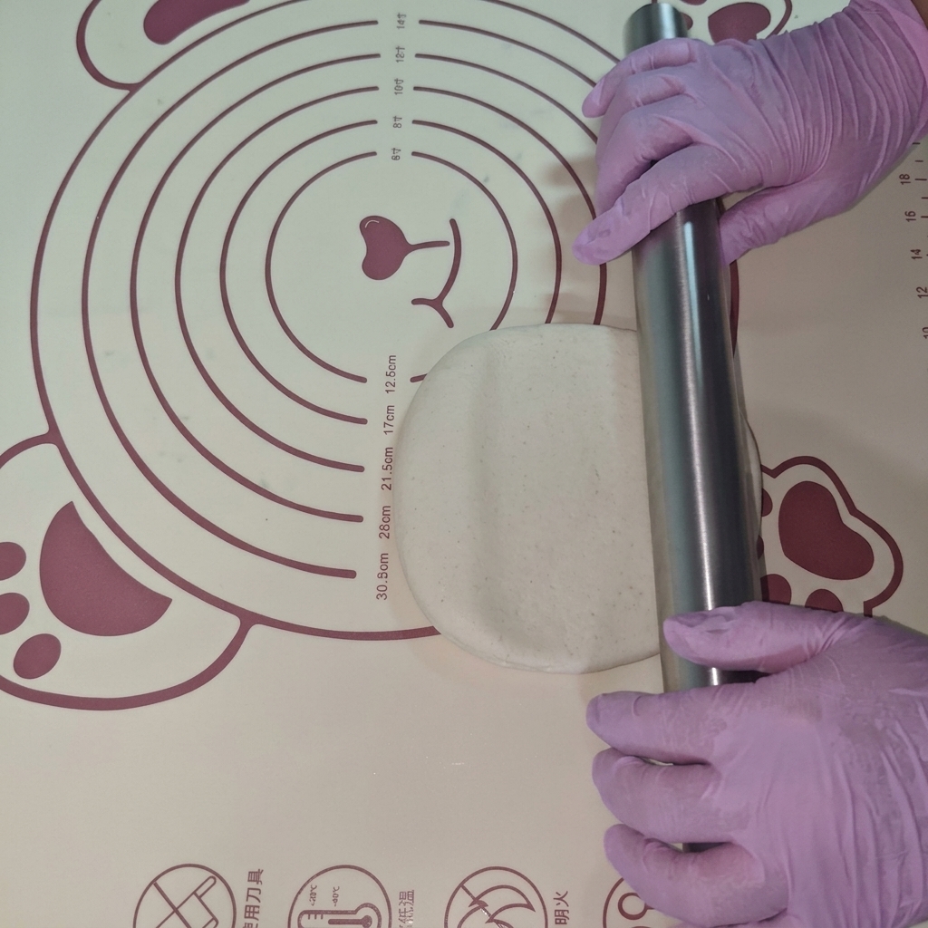 Un morceau de pâte étalé en un cercle plat sur un tapis en silicone à laide dun rouleau à pâtisserie.