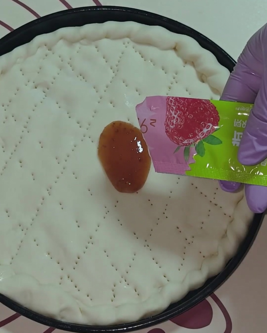 Gros plan sur une main gantée de violet étalant de la confiture de fraises rouge sur la pâte à pizza circulaire.