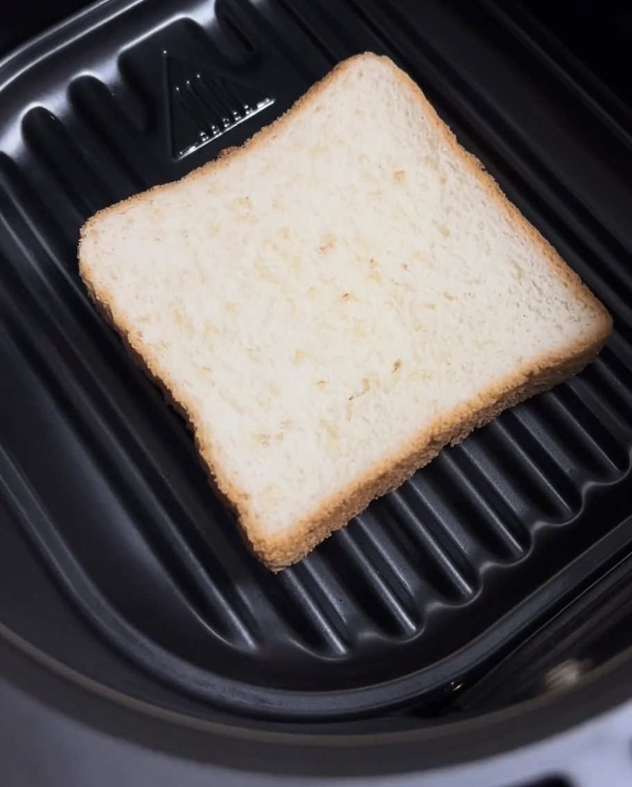 Une tranche de pain de mie nature posée à plat au fond du panier dun Air Fryer.