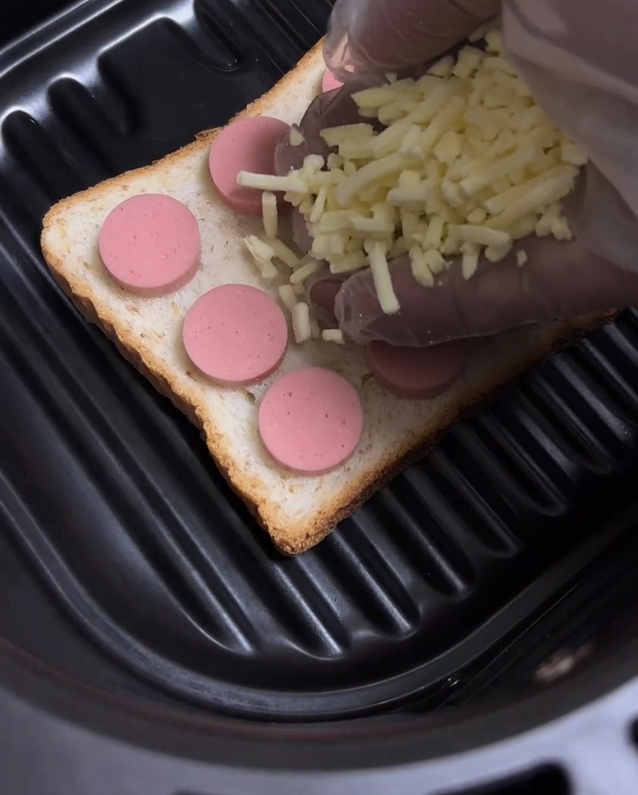 Du fromage jaune râpé saupoudré sur les rondelles de saucisse du toast.