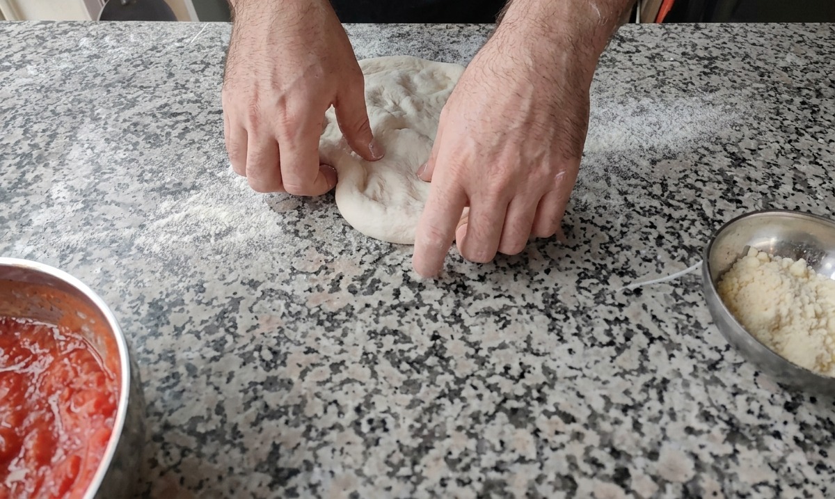 Deux mains pressant le centre dune boule de pâte à pizza sur un plan de travail fariné.