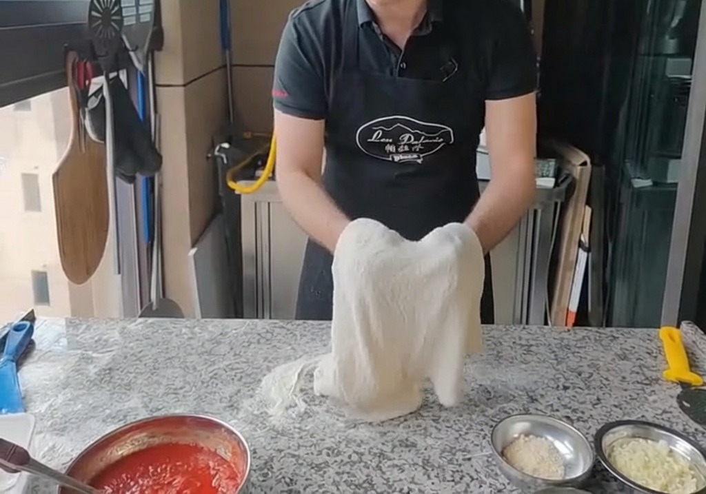 Étirement de la pâte à pizza sur le dos des deux mains, tenue verticalement.