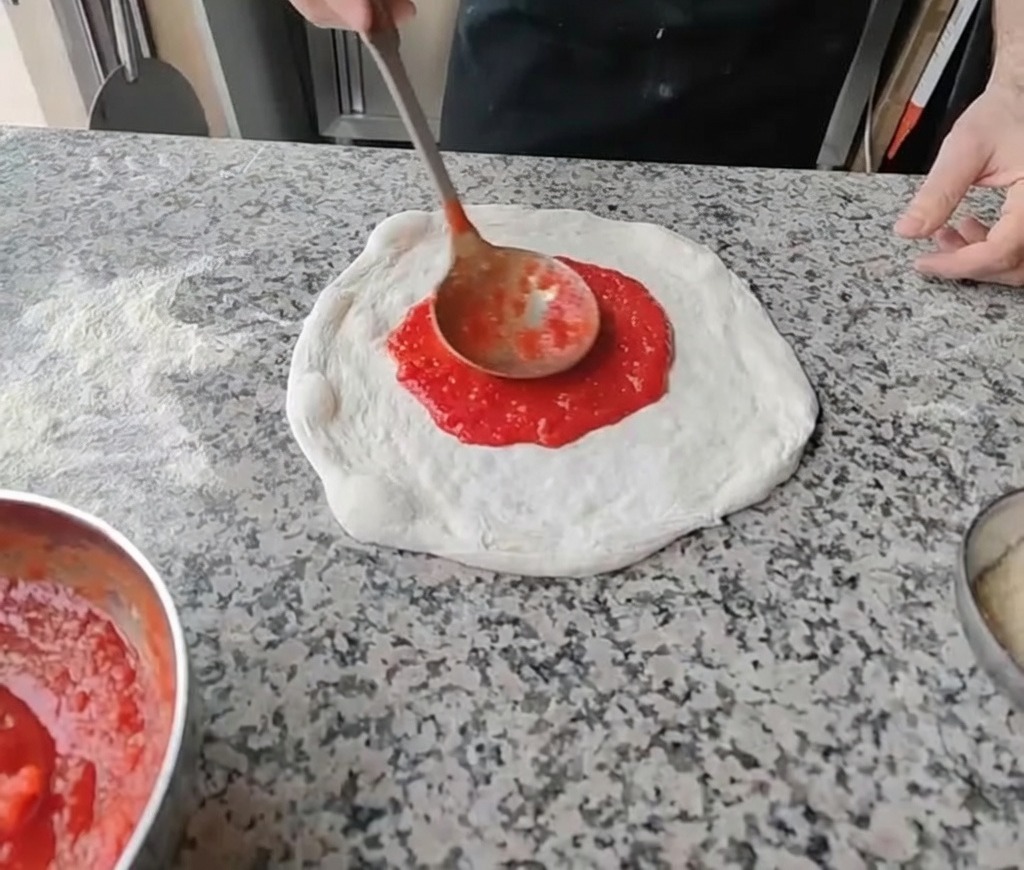 Étaler de la sauce tomate rouge vif au centre de la pâte à pizza étalée avec une louche.