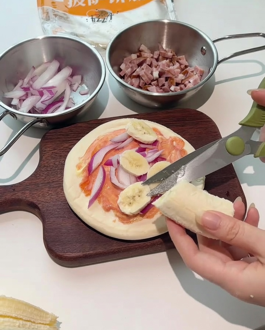 Des ciseaux de cuisine coupant directement des rondelles de banane sur la pizza.