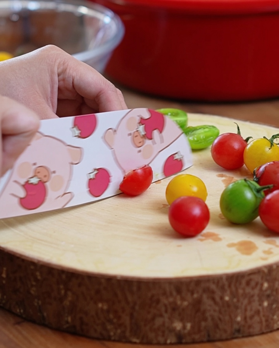 Tomates cerises coupées en deux sur une planche à découper en bois avec un couteau à motifs.