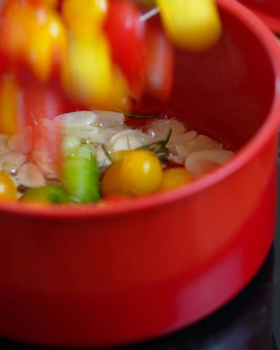 Tomates cerises coupées ajoutées dans une casserole dhuile chaude et dherbes.