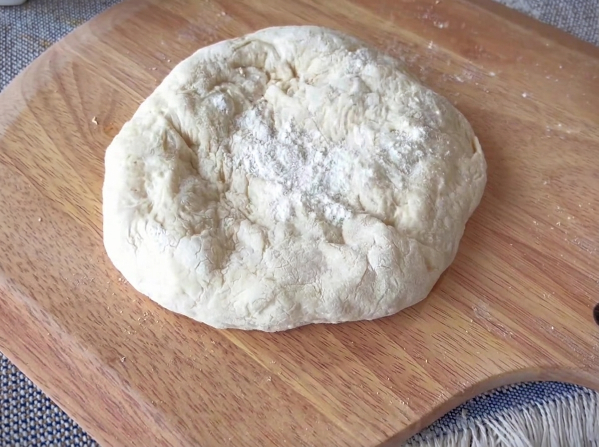 Un disque de pâte à pizza étalé sur une surface en bois, avec un rebord épais bien défini.