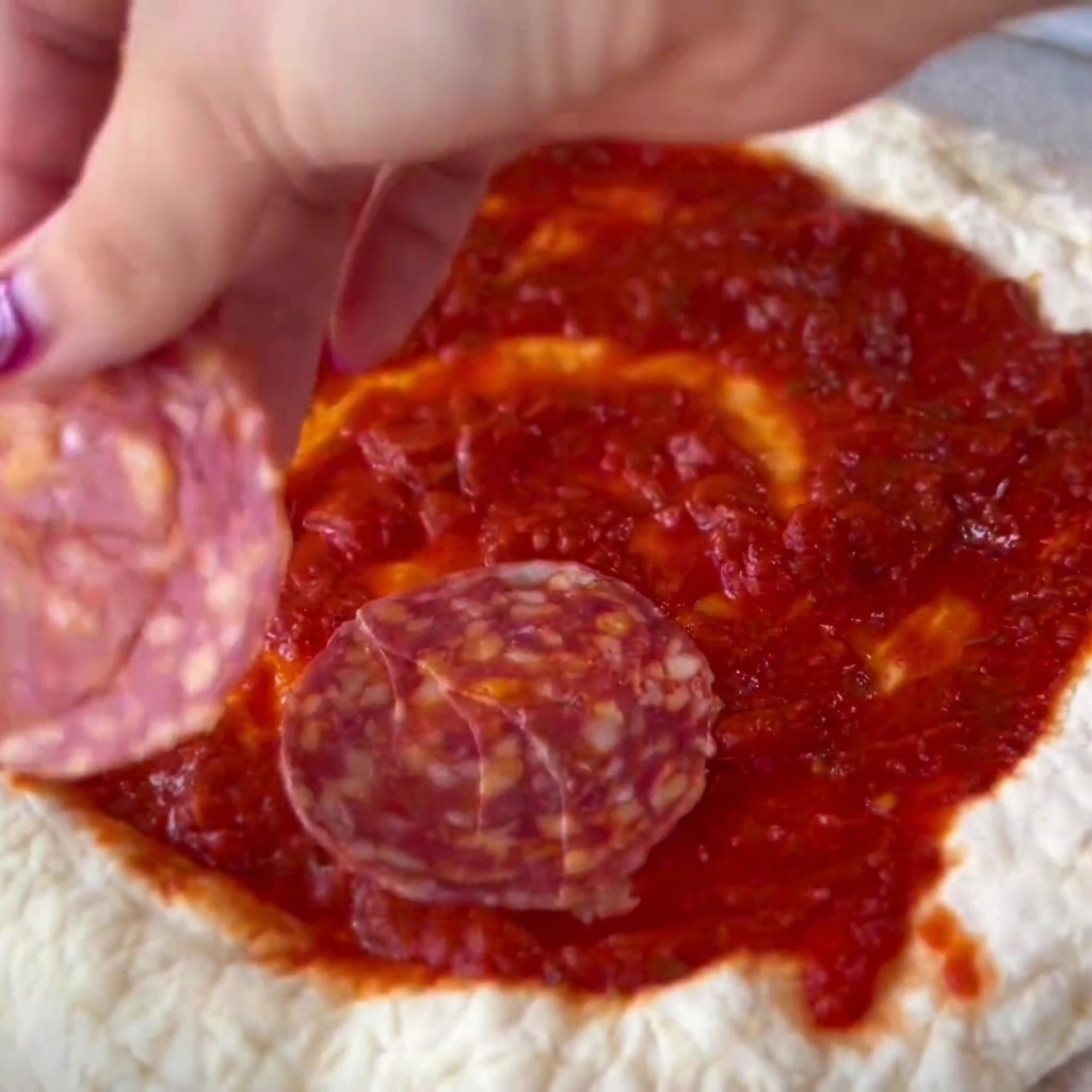 Des tranches de salami soigneusement placées sur le centre garni de sauce de la pâte à pizza.