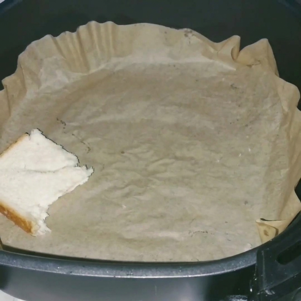 Gros plan sur des tranches de pain de mie disposées soigneusement dans un panier dAir Fryer recouvert de papier sulfurisé.