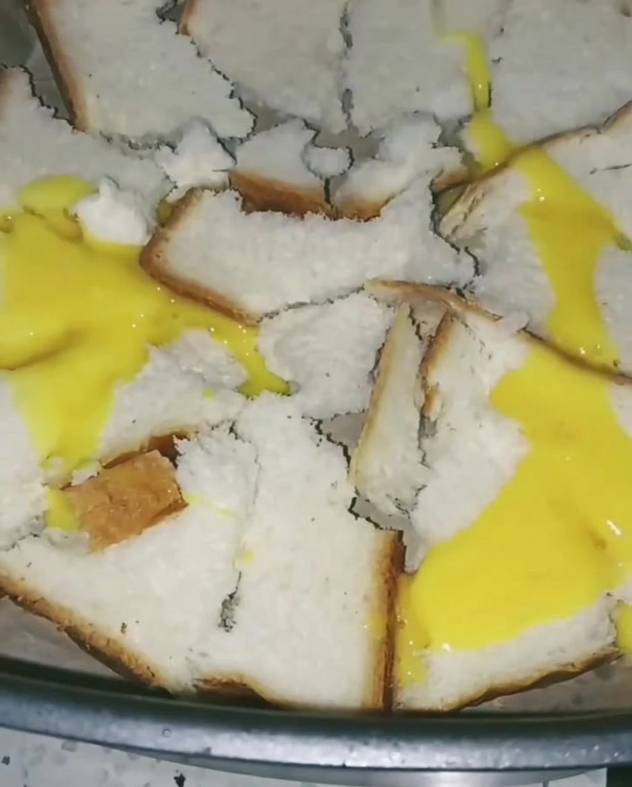 Des œufs battus versés sur le pain dans lAir Fryer, créant une fine couche jaune sur les tranches.