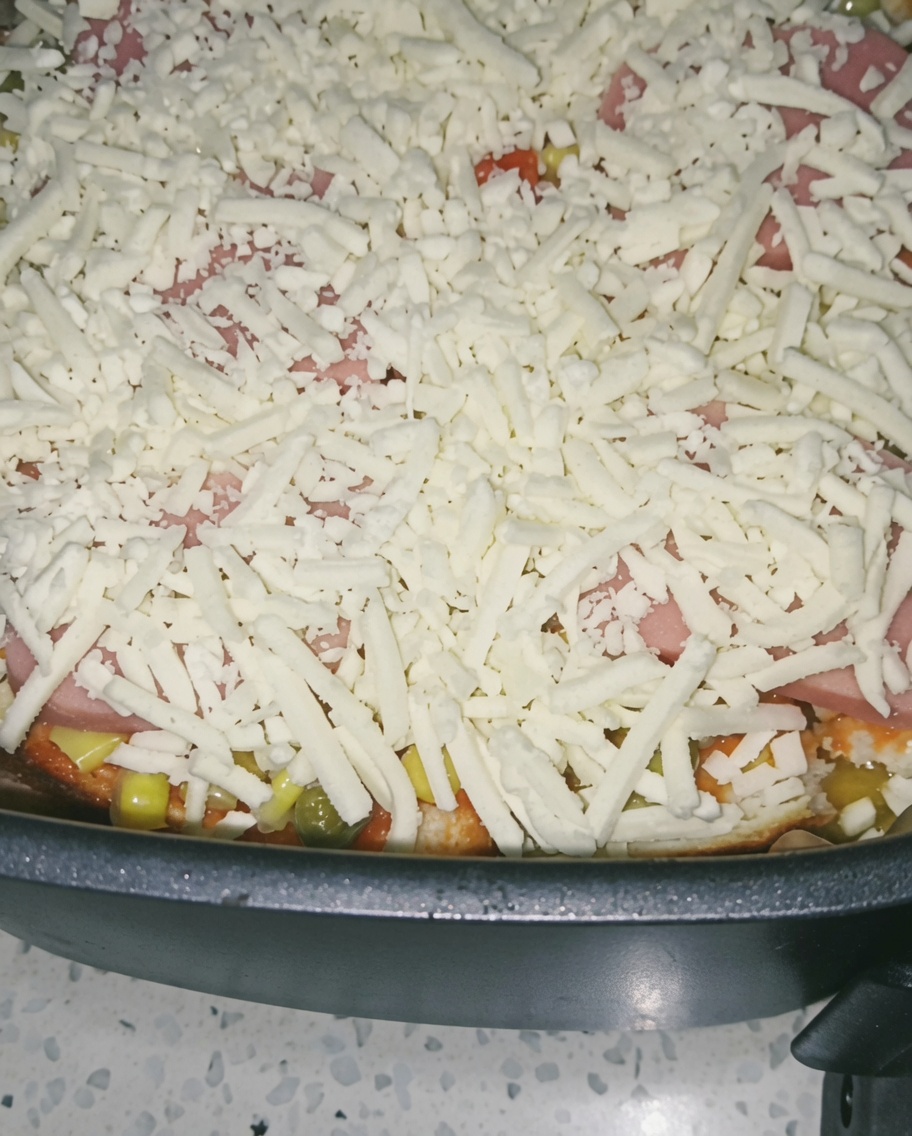 Gros plan sur une généreuse couche de fromage râpé recouvrant le jambon et les légumes dans le panier de lAir Fryer.