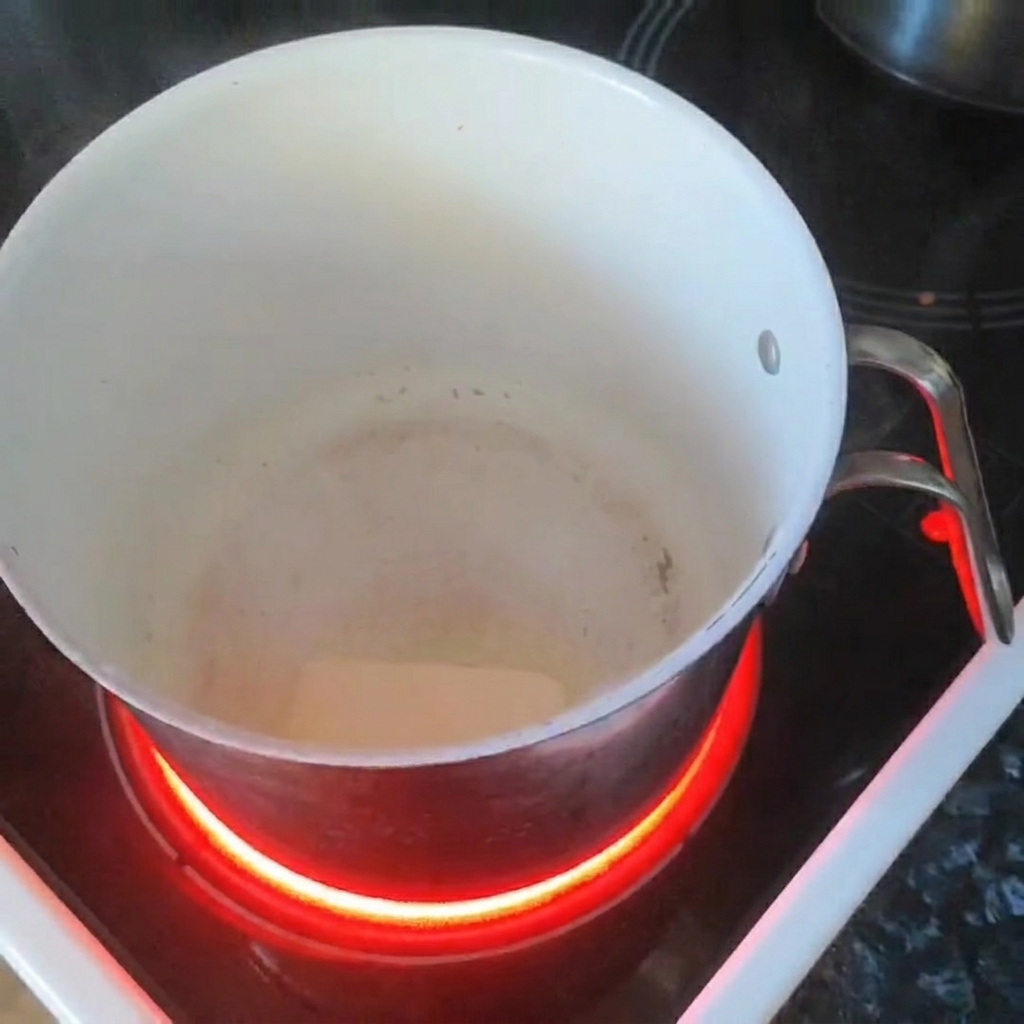 Une noisette de beurre fondant dans une casserole blanche sur une plaque à induction.