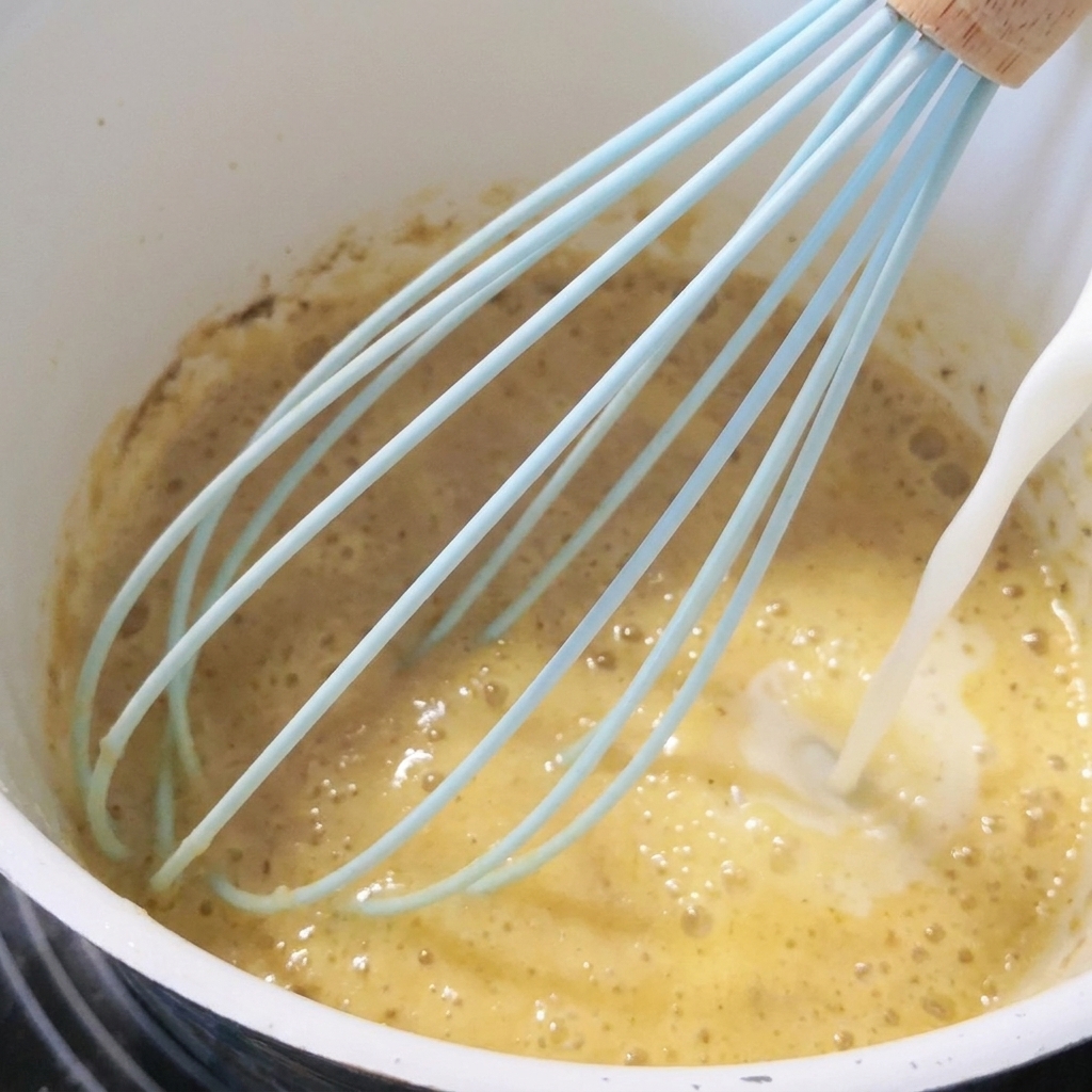 Le lait est versé dans le roux tout en fouettant.