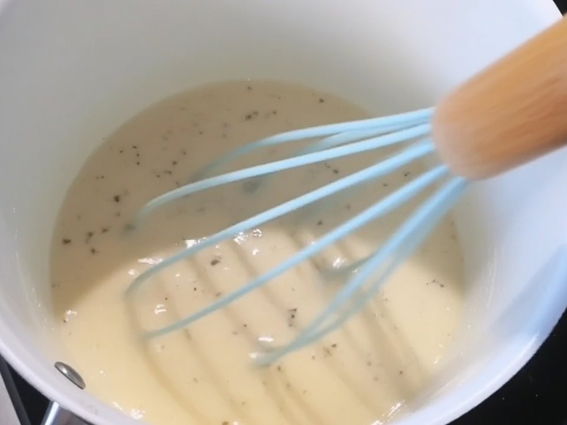 Le sel, le poivre noir et le fromage râpé sont ajoutés à la sauce blanche crémeuse.