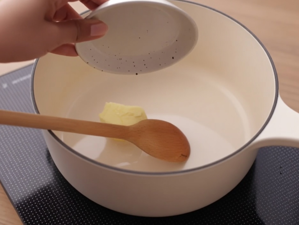 Une noix de beurre fondant dans une casserole blanche propre sur une cuisinière.