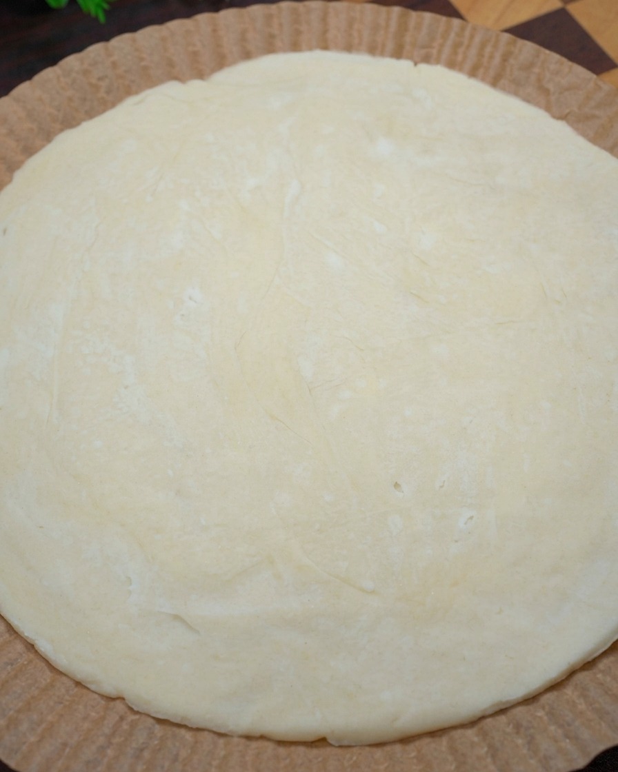Gros plan de mains façonnant les bords dune crêpe à la ciboule crue sur du papier sulfurisé pour former une croûte à pizza.