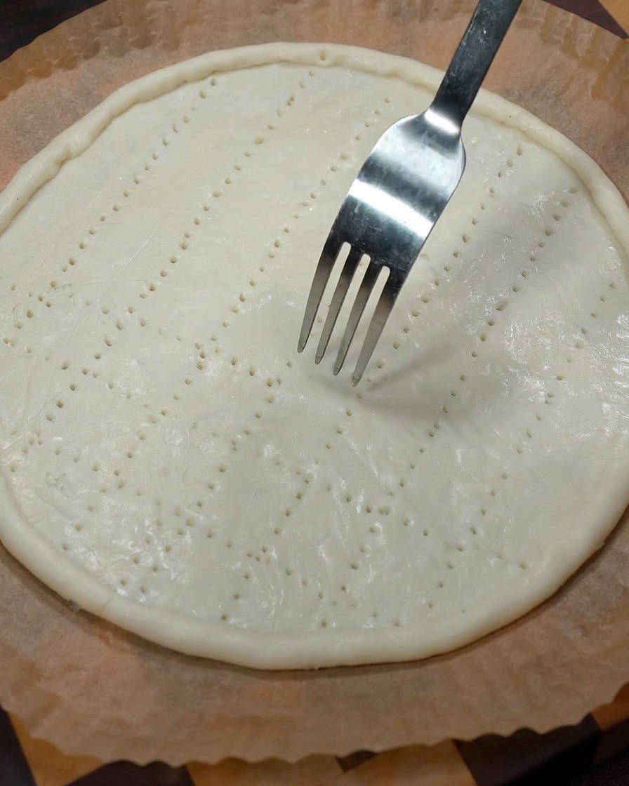 Une fourchette en métal pique la base de la pâte crue pour créer des petits trous de ventilation.