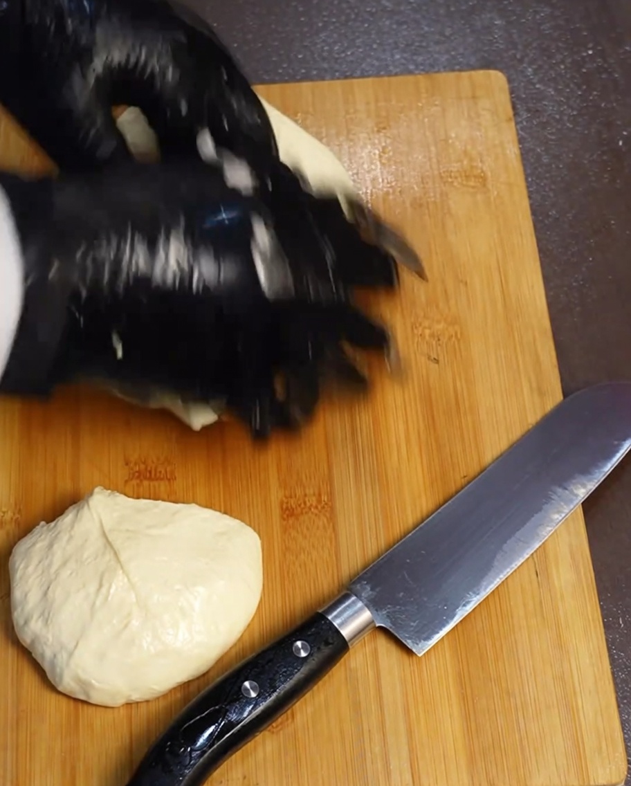 Quatre portions égales de pâte à pizza reposant sur une planche à découper en bois à côté dun couteau.